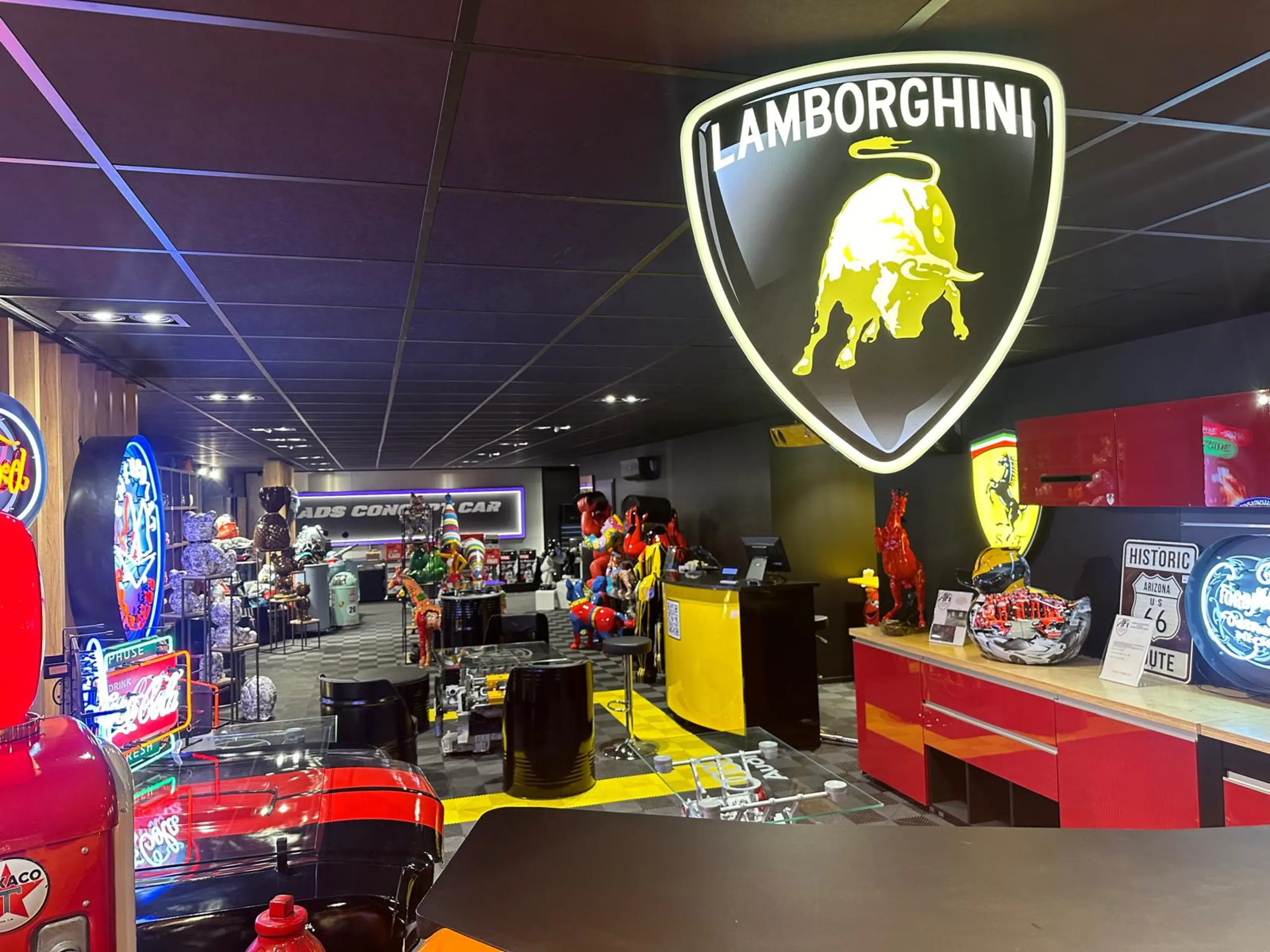La boutique ADS Concept Store à l’étage du showroom : enseigne lumineuse Lamborghini, néons vintage, comptoir rouge et allée de pièces de collection