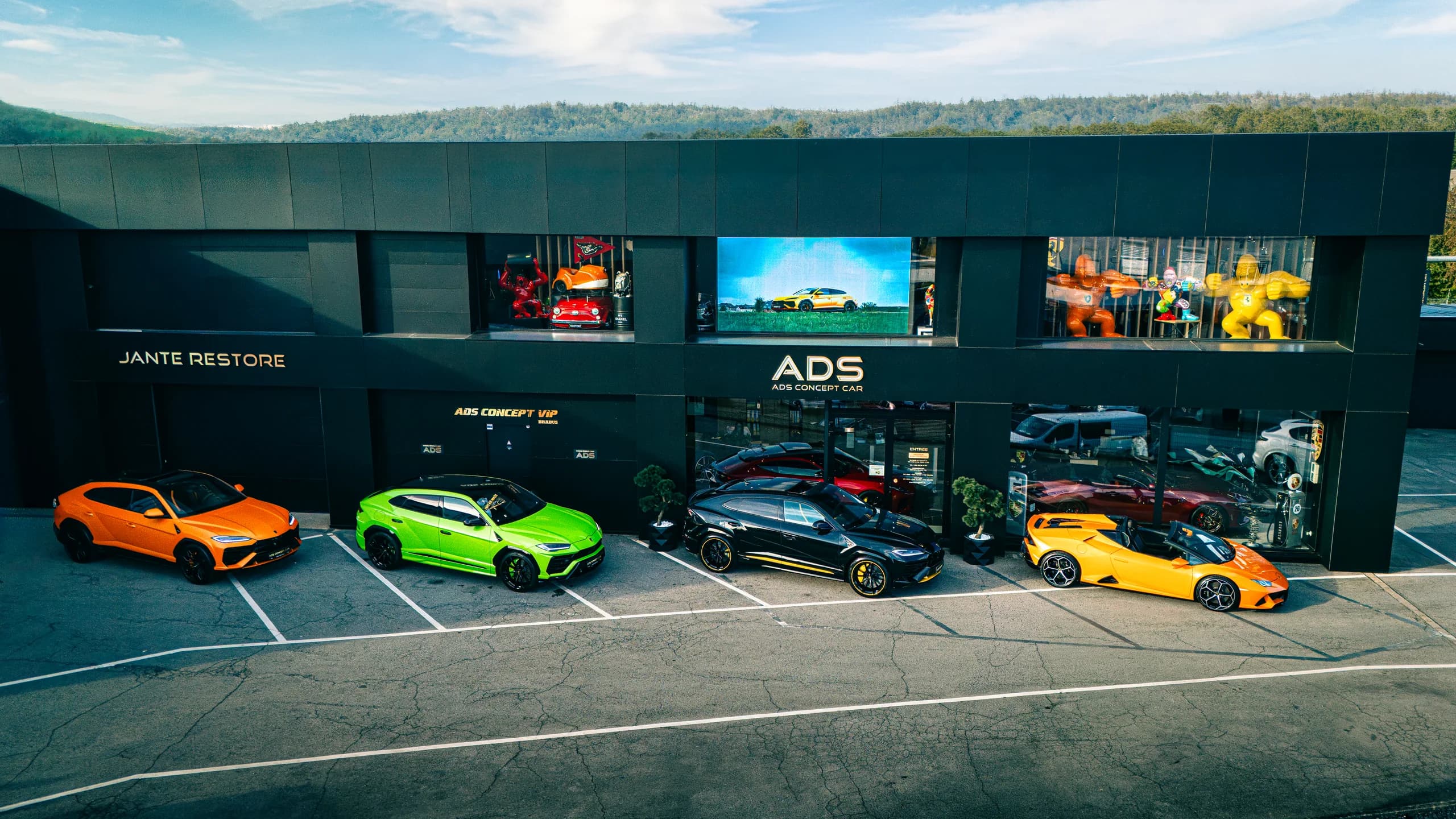 Le showroom ADS Concept Car à Foetz vu du ciel : façade noire, enseignes ADS et Jante Restore, quatre Lamborghini devant les vitrines